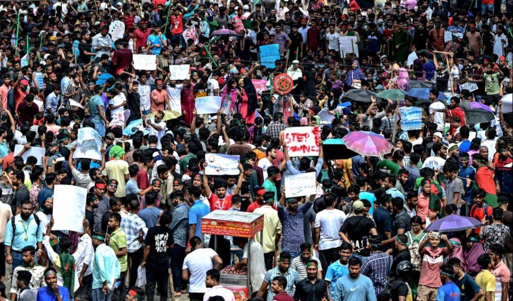 Protesters wave national flags as they stand over the Anti Terrorism Raju Memorial Sculpture during a protest in Dhaka on August 4, 2024, to demand justice for the victims arrested and killed in the recent nationwide violence during anti-quota protests. The death toll from clashes on August 4 between Bangladeshi protesters demanding Prime Minister Sheikh Hasina resign and pro-government supporters has risen to at least 23, police and doctors said. (Photo by Munir UZ ZAMAN / AFP)